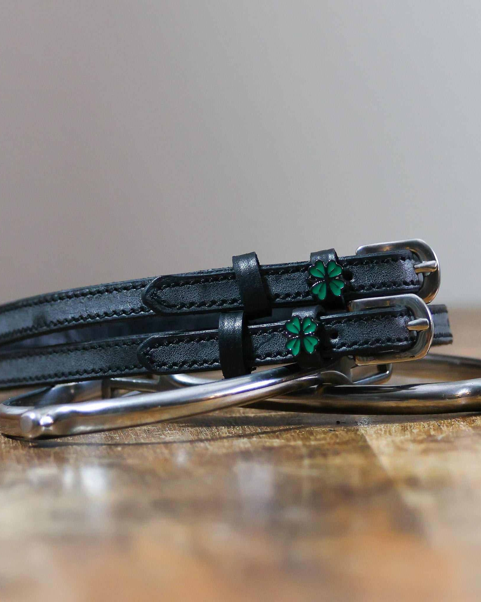 Coiled black leather clover spur straps resting on a silver spur, green four leaf clover charms