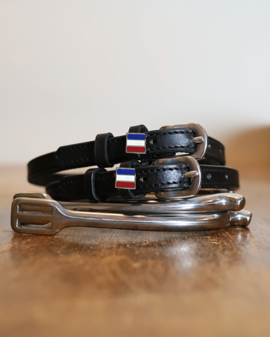Coiled black leather French flag spur straps stacked on a spur on a wooden table