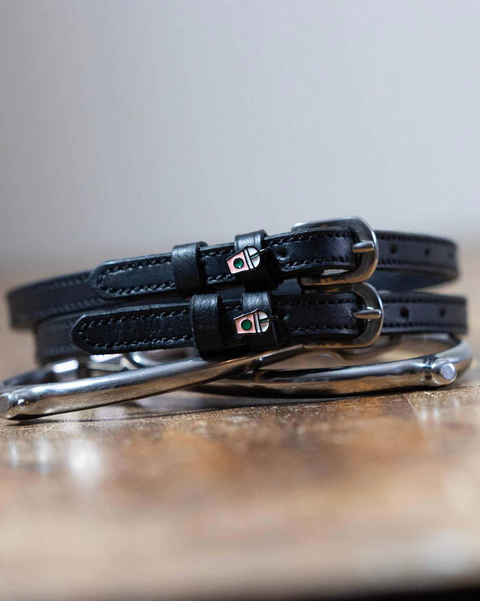 Coiled black leather spur straps and a silver spur on wood with frappe cup charms