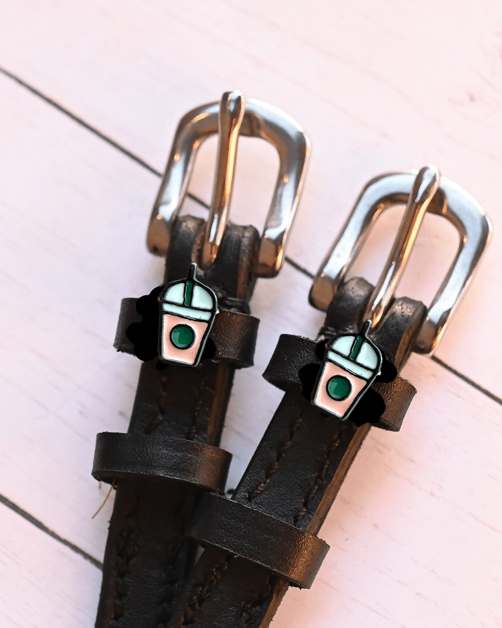 Close-up of frappe cup charms and silver buckles on black spur straps, pink planks