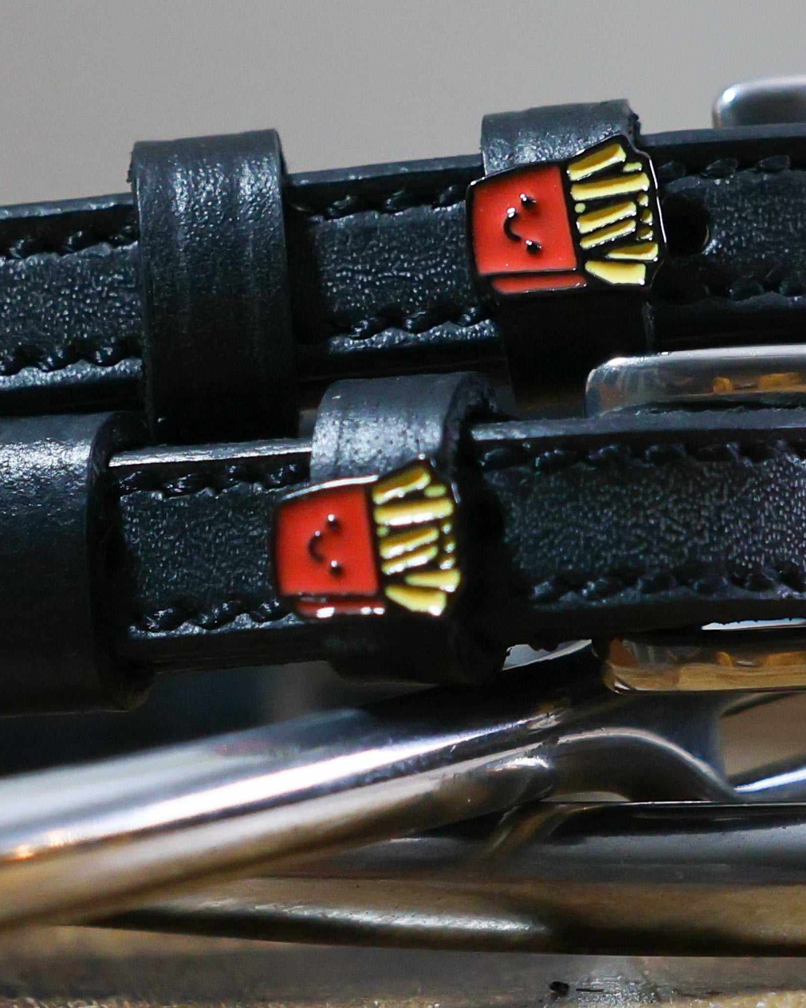 Close-up of smiling French fry charms on black leather spur straps over spur hardware