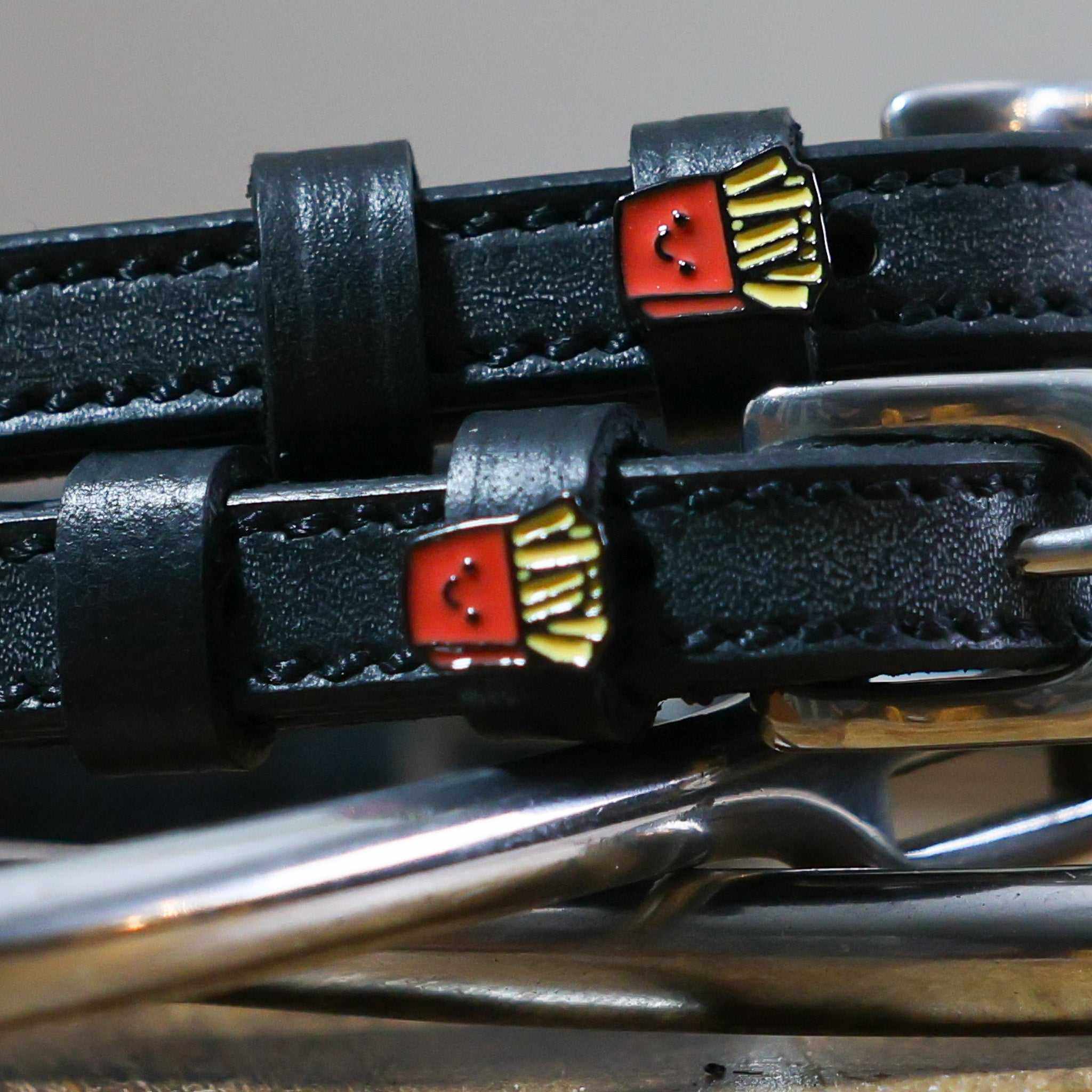 Close-up of smiling French fry charms on black leather spur straps over spur hardware