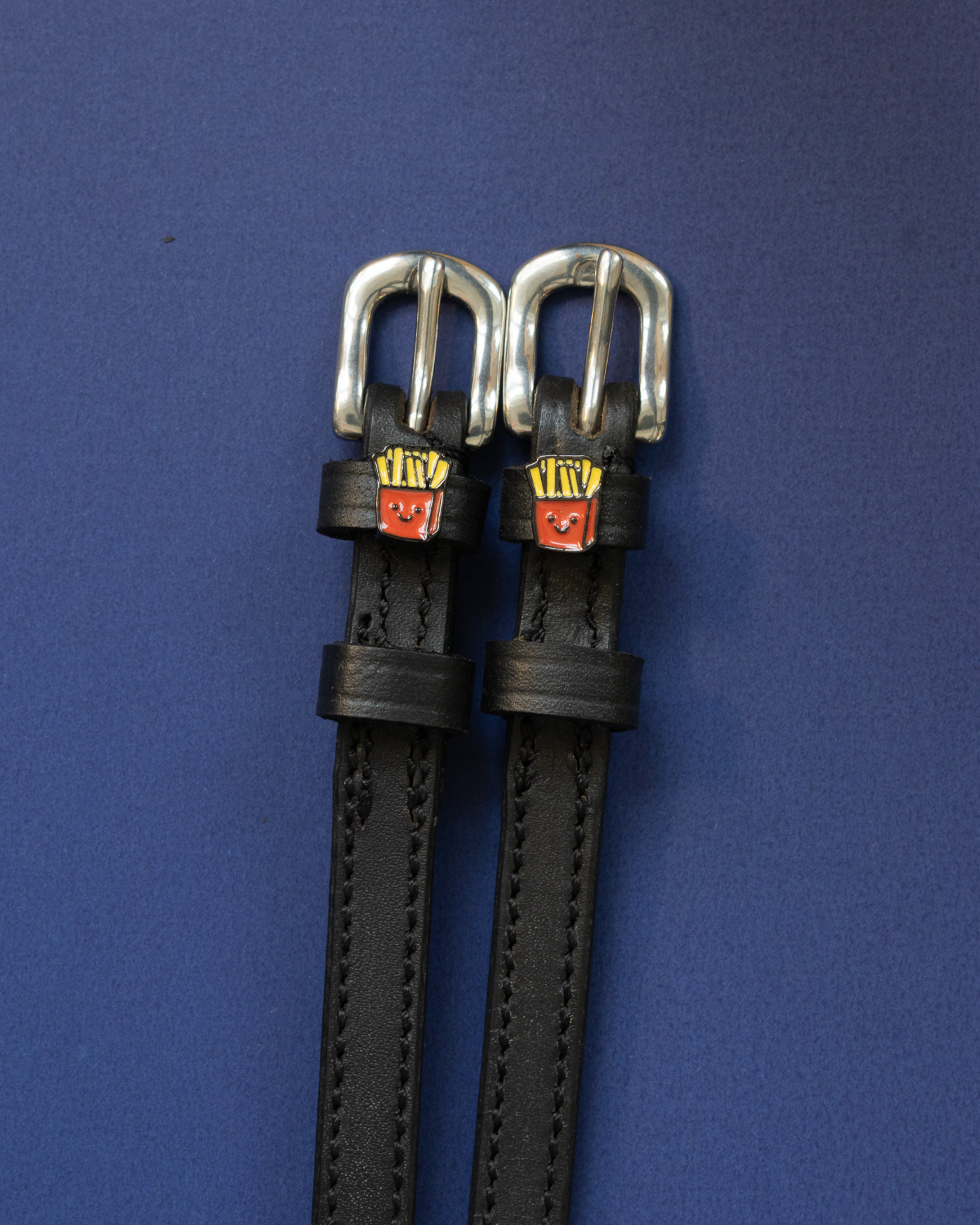 Pair of black leather French Fries spur straps with silver buckles on a navy background