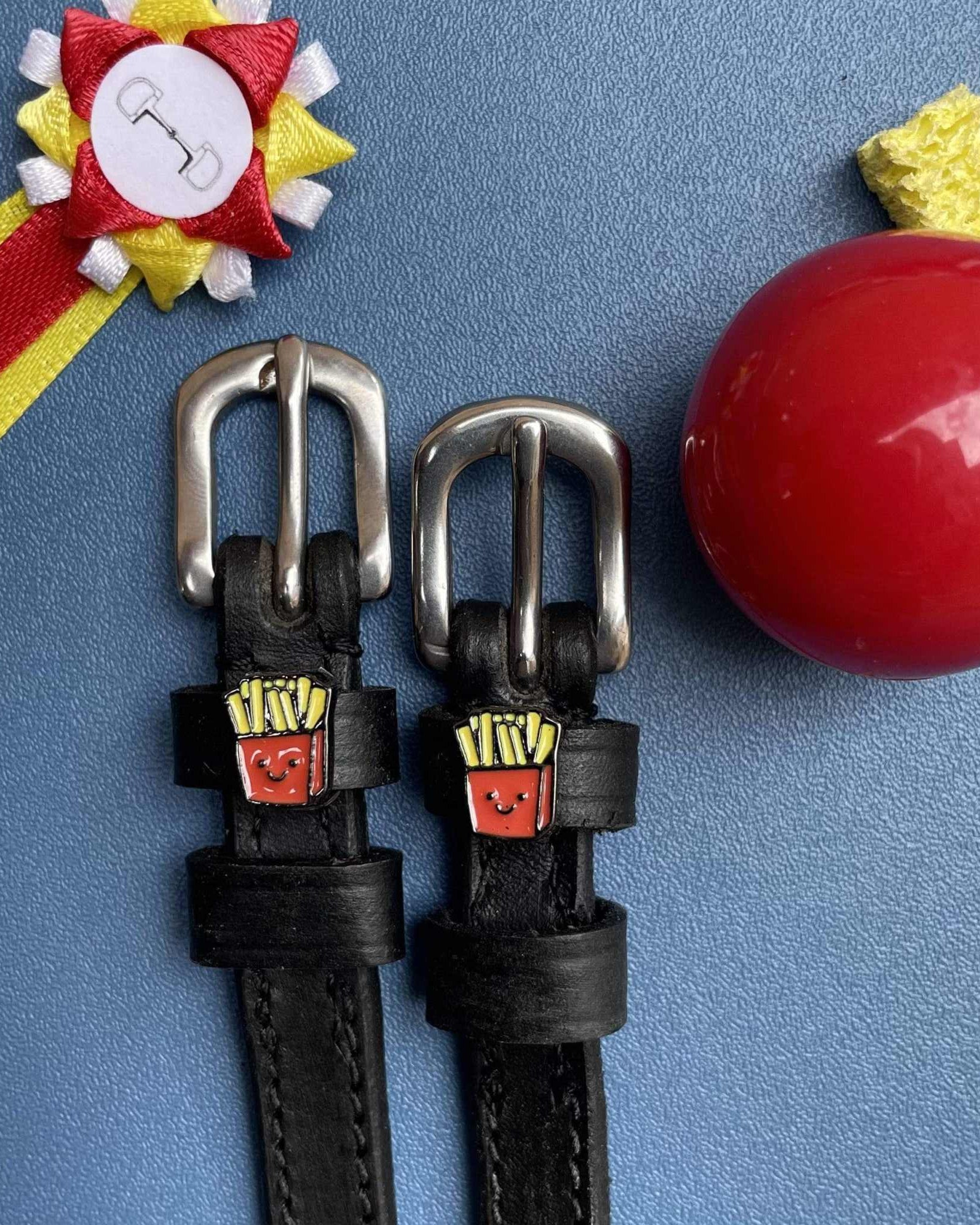 French Fries spur straps styled with a show rosette and red apple on a blue background