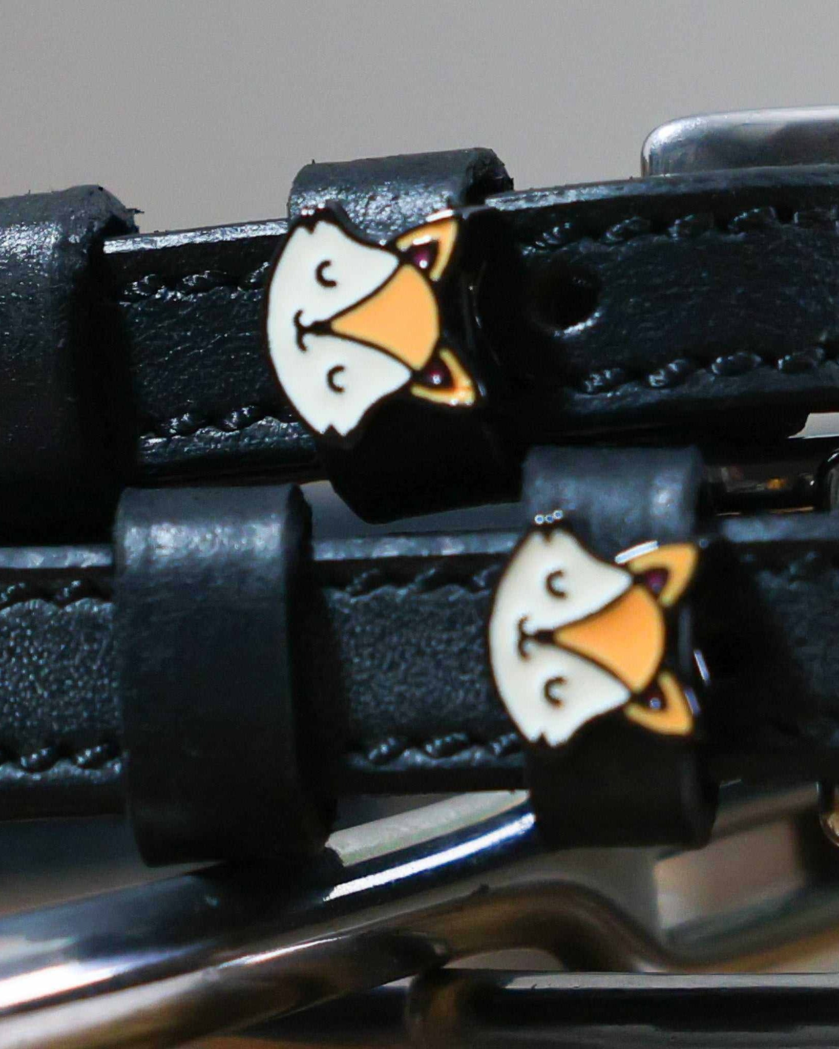 Close-up of orange fox face charms on the keepers of black leather spur straps