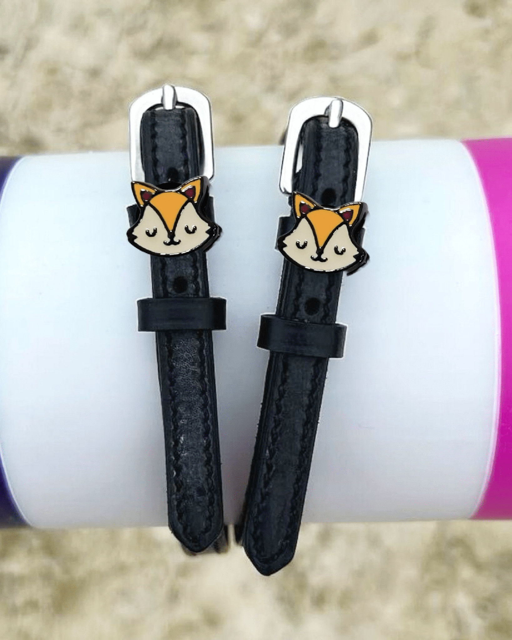 Black leather fox spur straps styled over colorful tumblers on sand by ManeJane