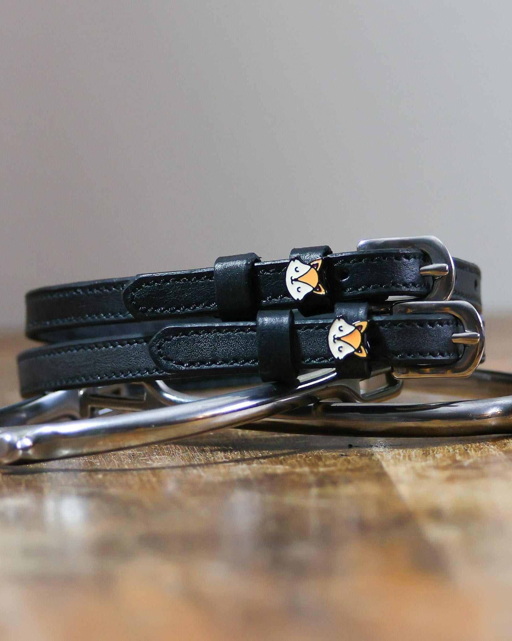 Coiled black leather ManeJane fox spur straps stacked on a silver spur on wood