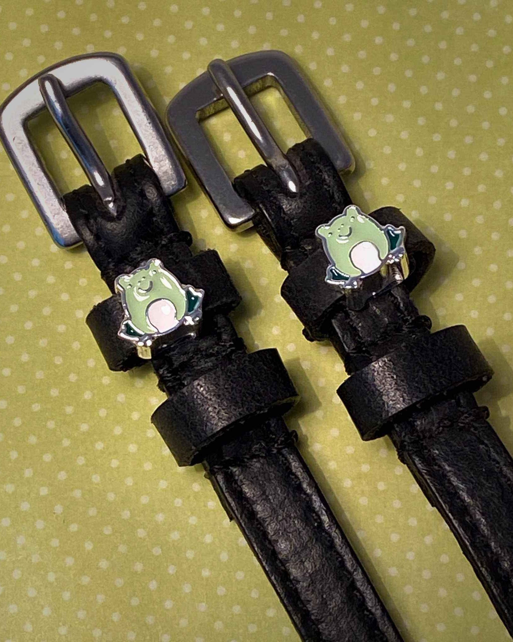 Black leather frog spur straps with silver buckles on a green polka-dot background