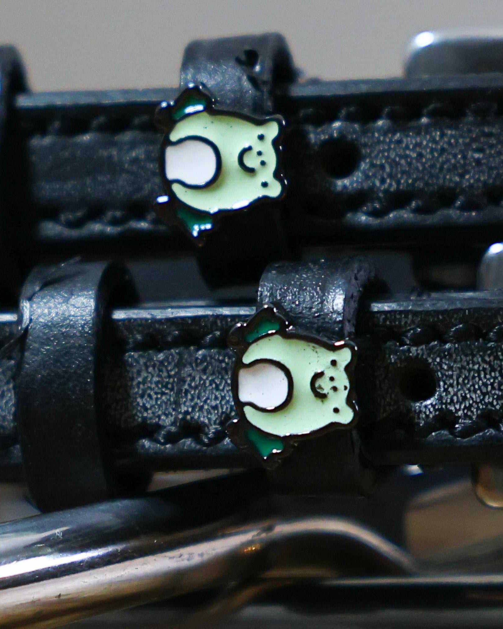 Close-up of green enamel frog charms on the keepers of black leather ManeJane spur straps
