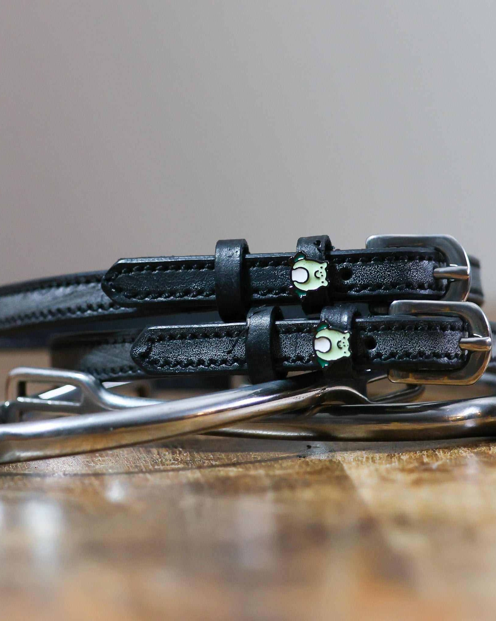 Black leather frog spur straps coiled beside a silver stirrup on a rustic wooden surface