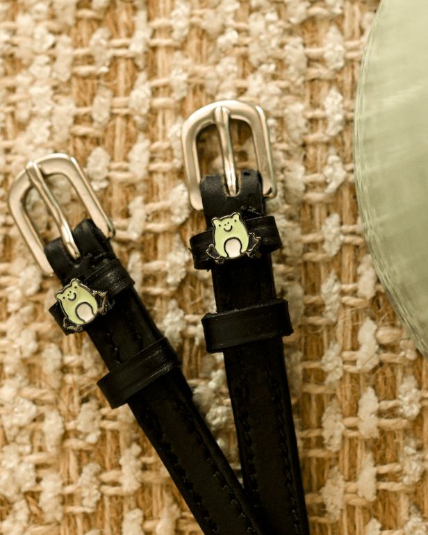Black leather frog spur straps with silver buckles angled on a woven jute background