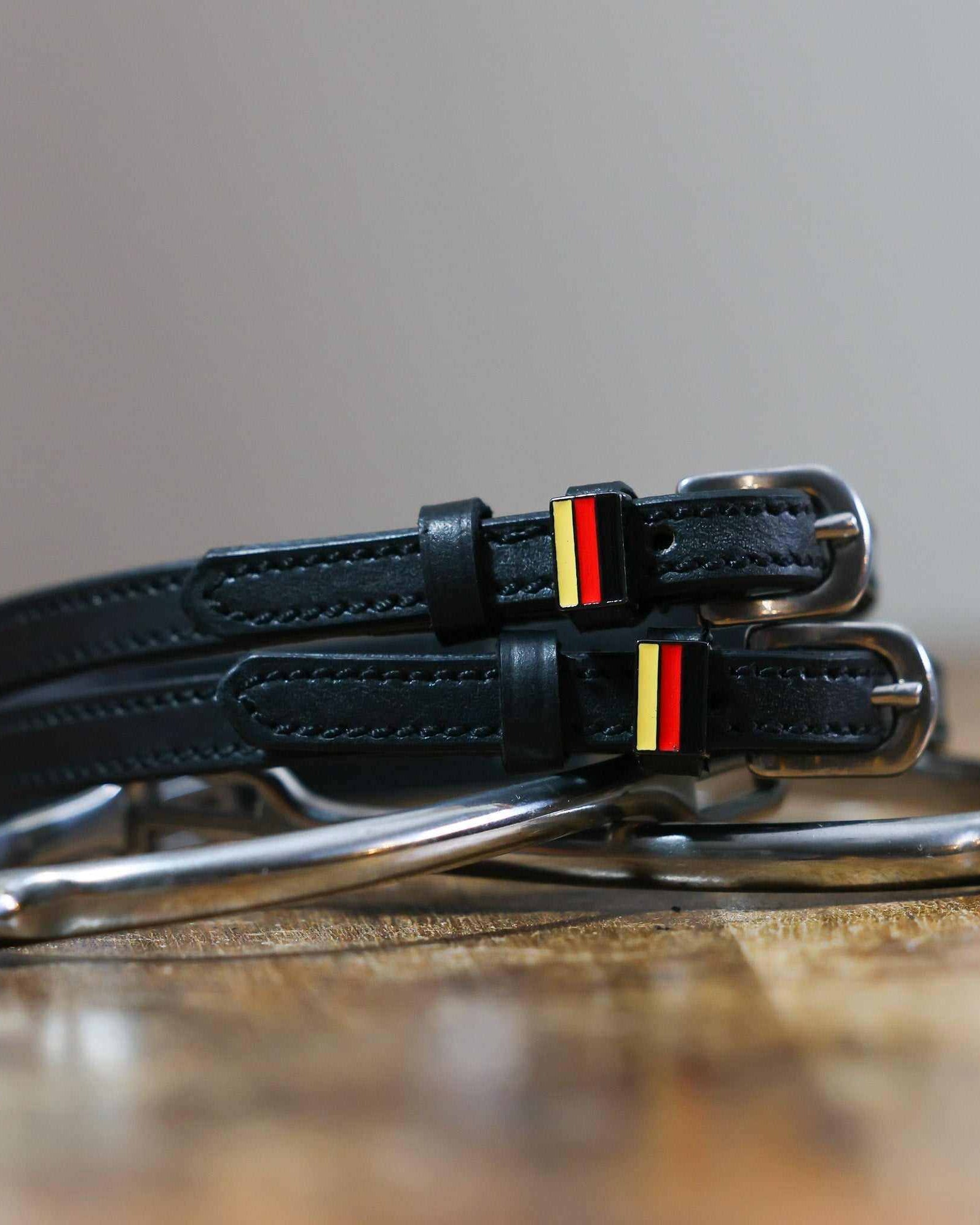 Black leather German flag spur straps coiled beside a silver spur on a wooden surface