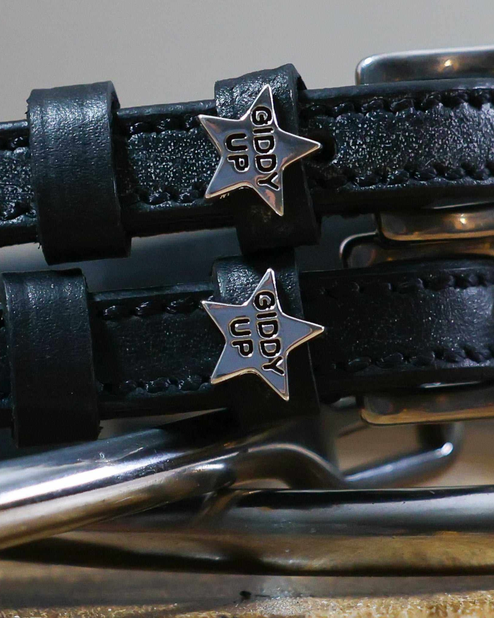 Close-up of silver 'Giddy Up' star charms on black leather spur strap keepers