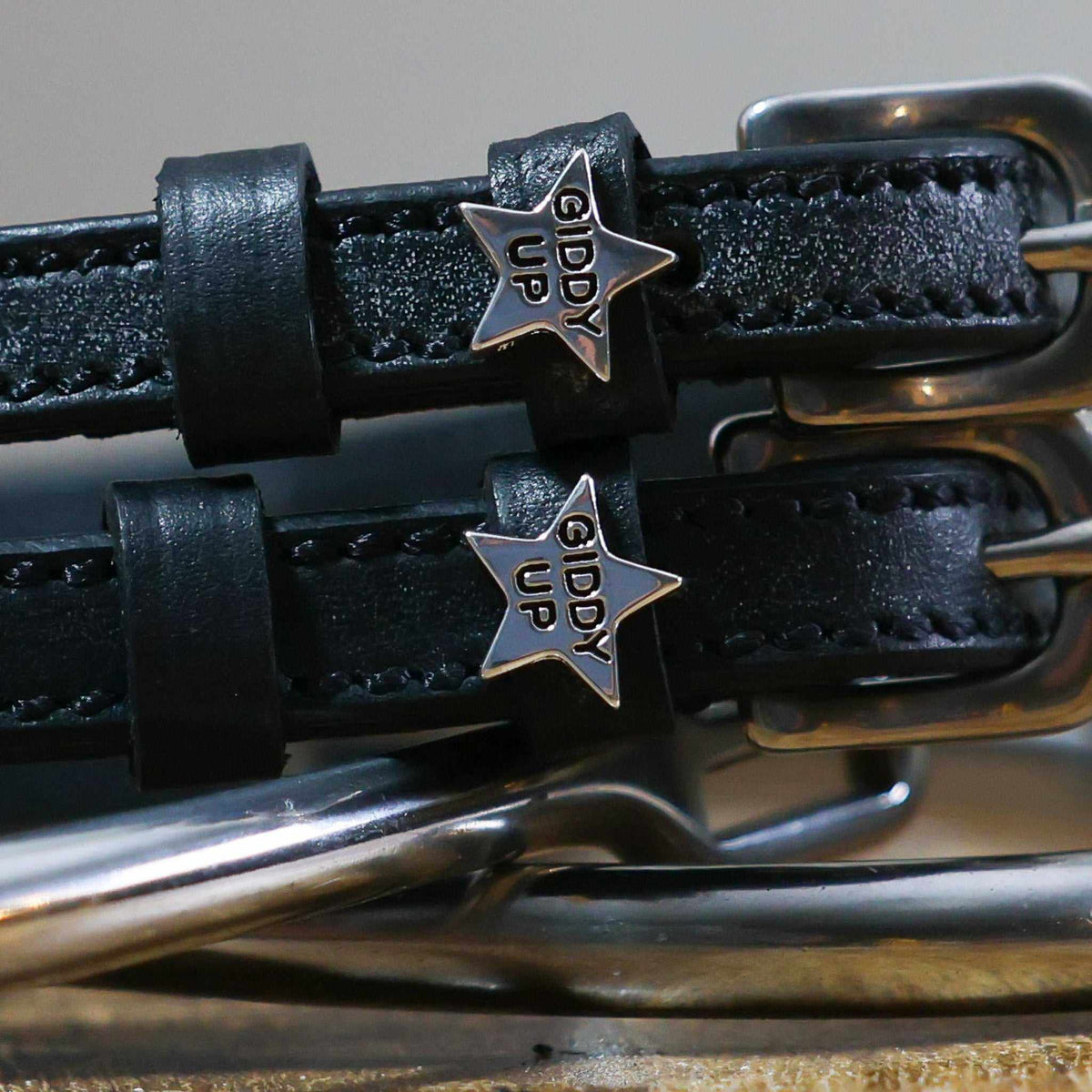 Close-up of silver 'Giddy Up' star charms on black leather spur strap keepers