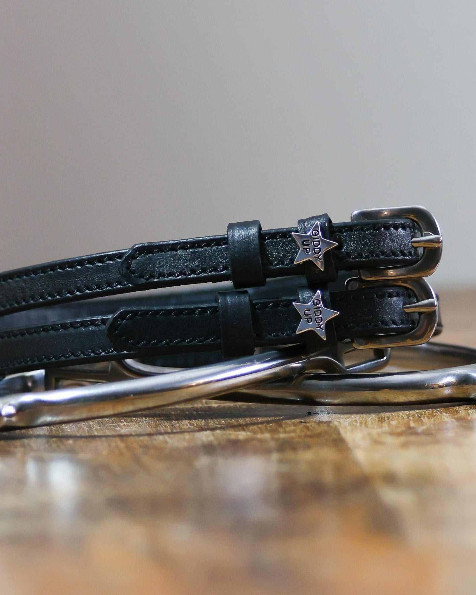Coiled black leather 'Giddy Up' spur straps stacked on a silver spur on a wooden table