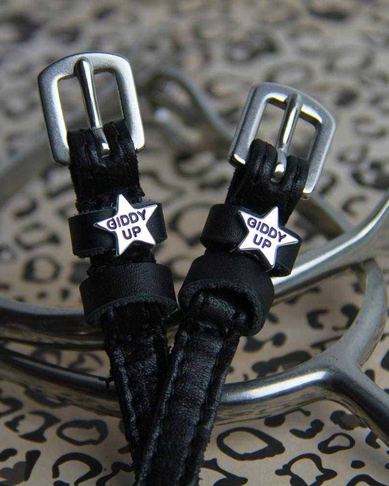 Close-up of black-enamel 'Giddy Up' star charms on spur straps over a leopard print
