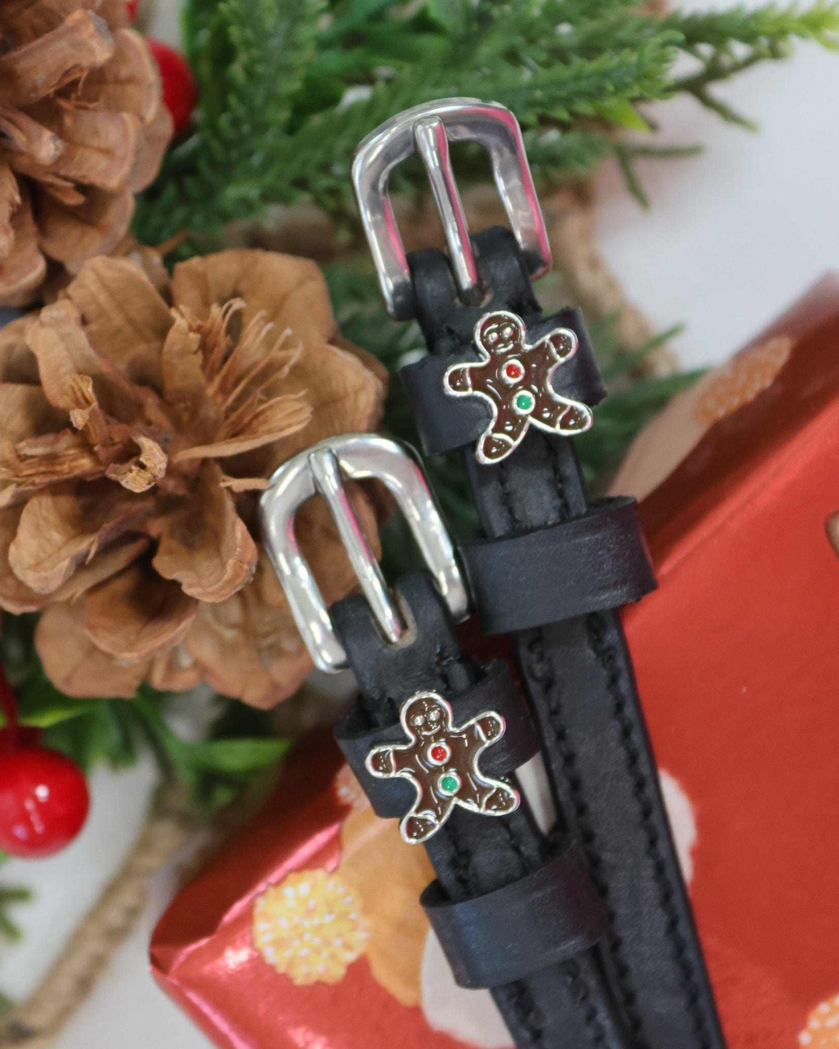 Gingerbread man spur straps styled with pinecones, holly and a red gift box