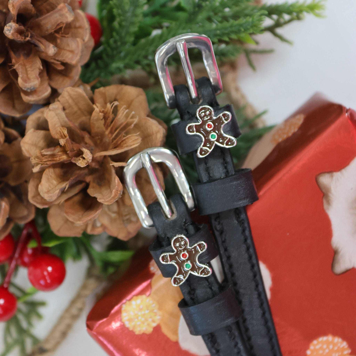 Gingerbread man spur straps styled with pinecones, holly and a red gift box