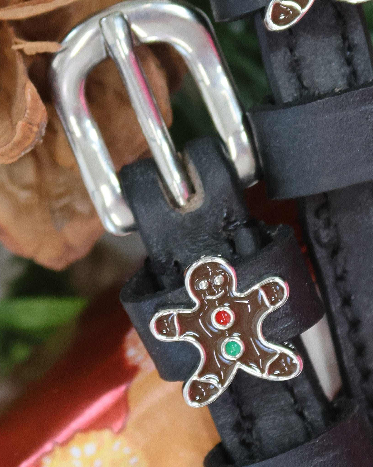 Close-up of an enamel gingerbread man charm on a black leather spur strap keeper
