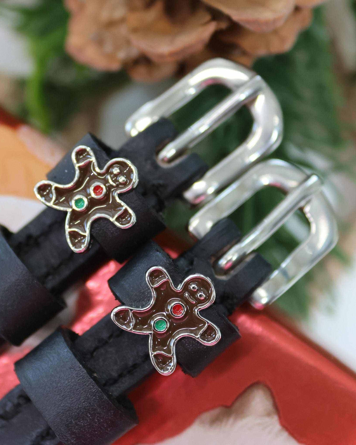 Gingerbread man charms on black spur straps beside pinecones and red gift wrap