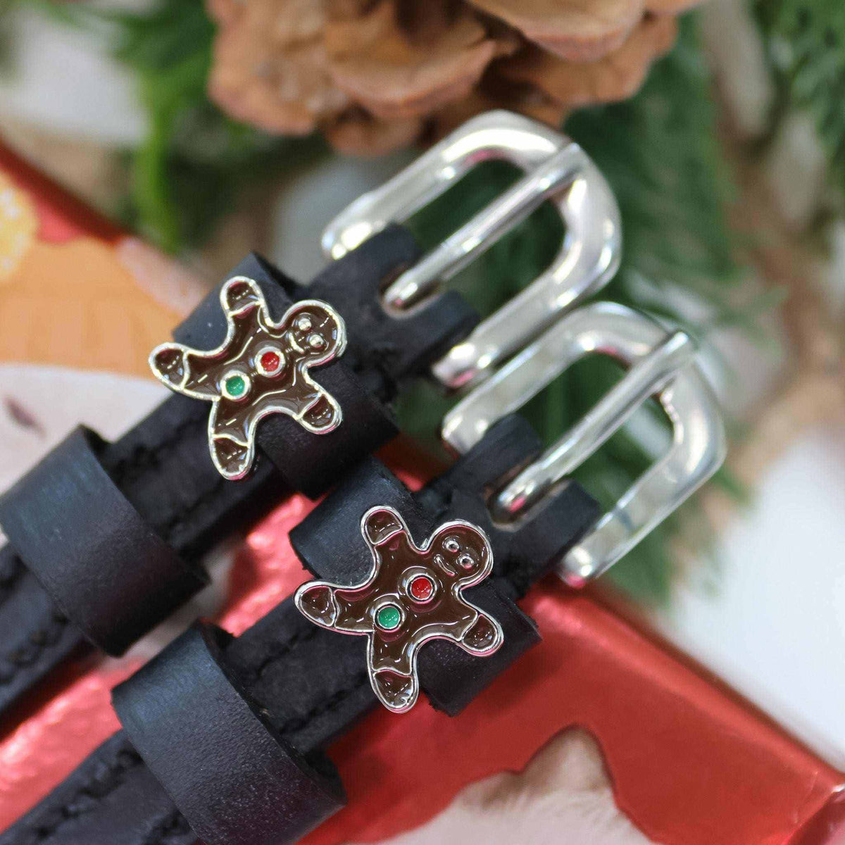 Gingerbread man charms on black spur straps beside pinecones and red gift wrap