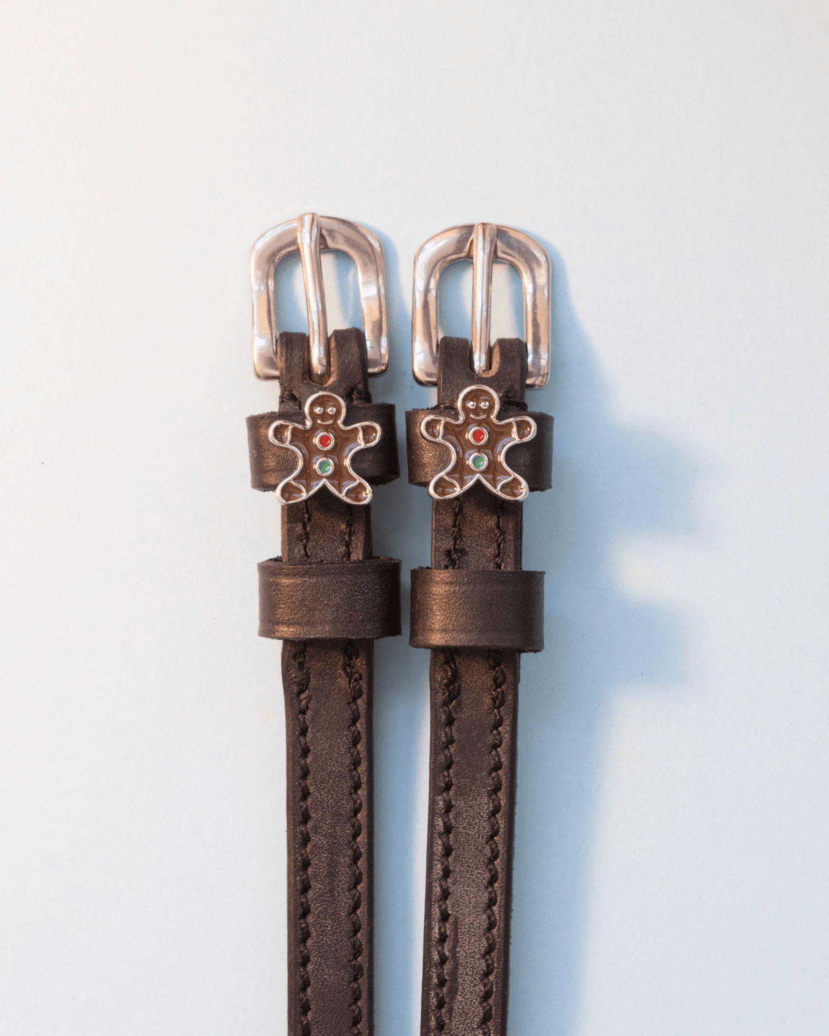 Dark brown leather gingerbread man spur straps with silver buckles on off-white
