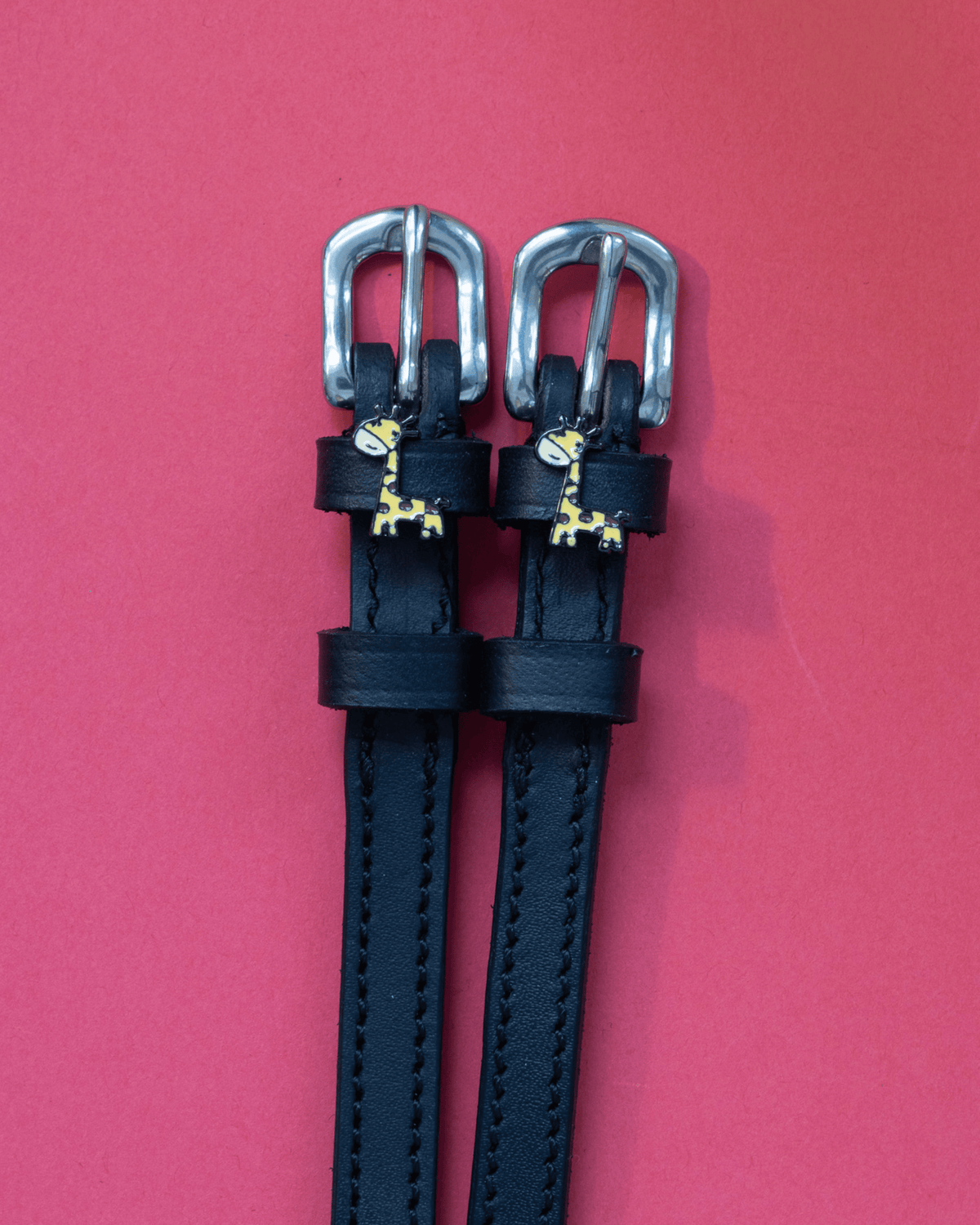 Black leather ManeJane Giraffe spur straps with silver buckles on a red background