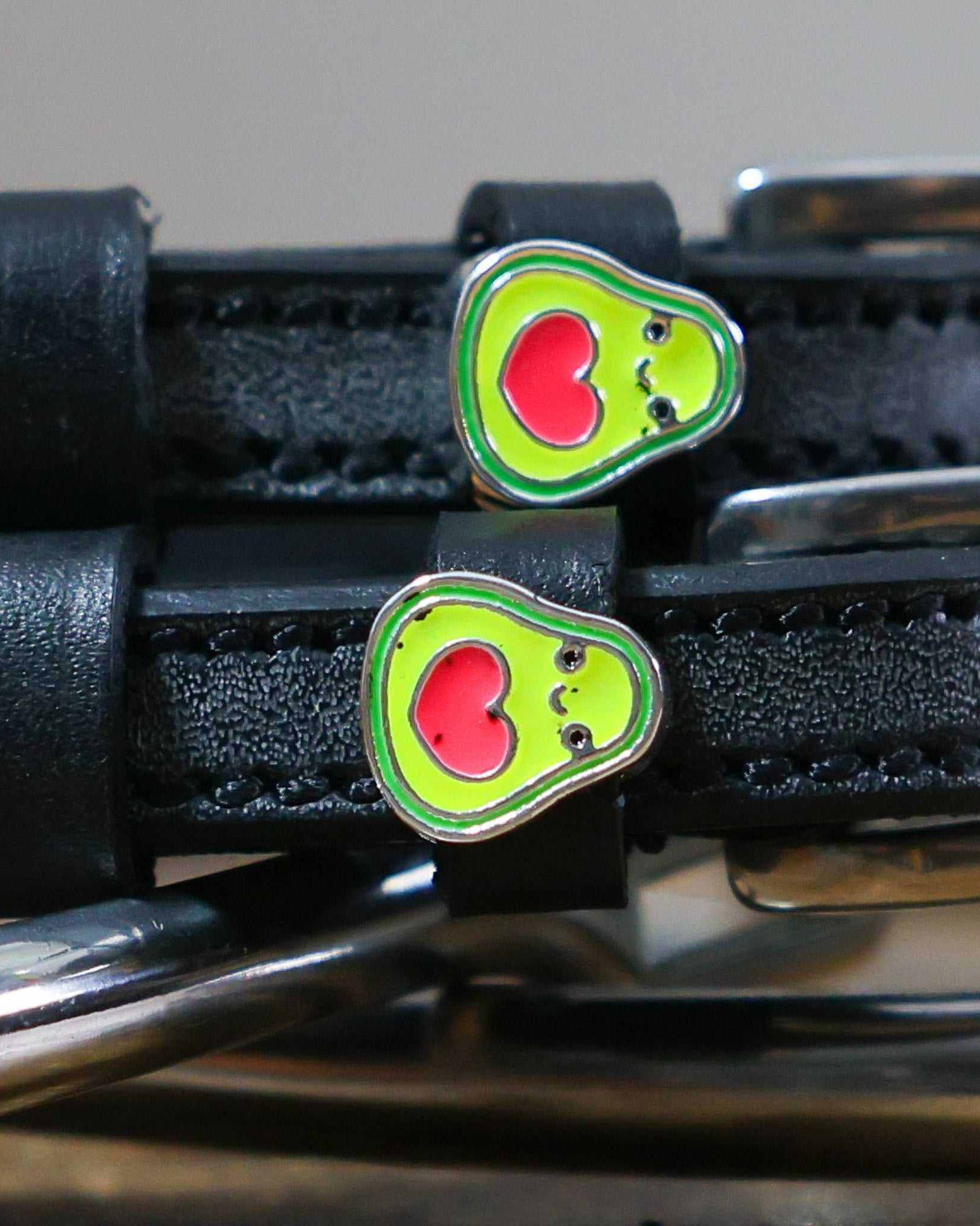 Close-up of green avocado charms with red heart pits on black spur strap keepers