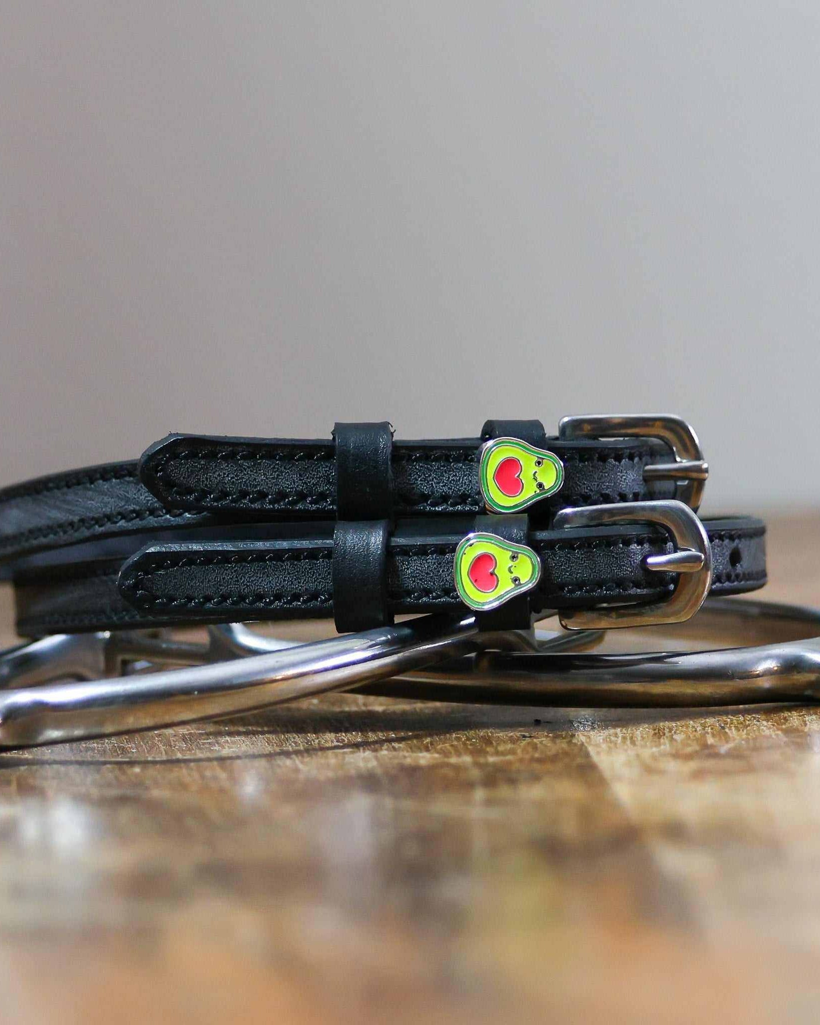 Coiled black leather spur straps and a silver spur on wood with avocado heart charms