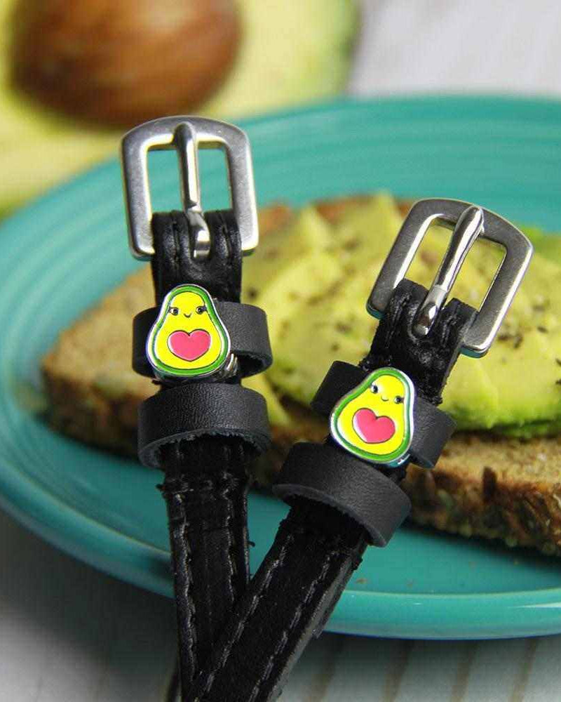 Avocado-charm ManeJane spur straps resting on avocado toast on a teal plate