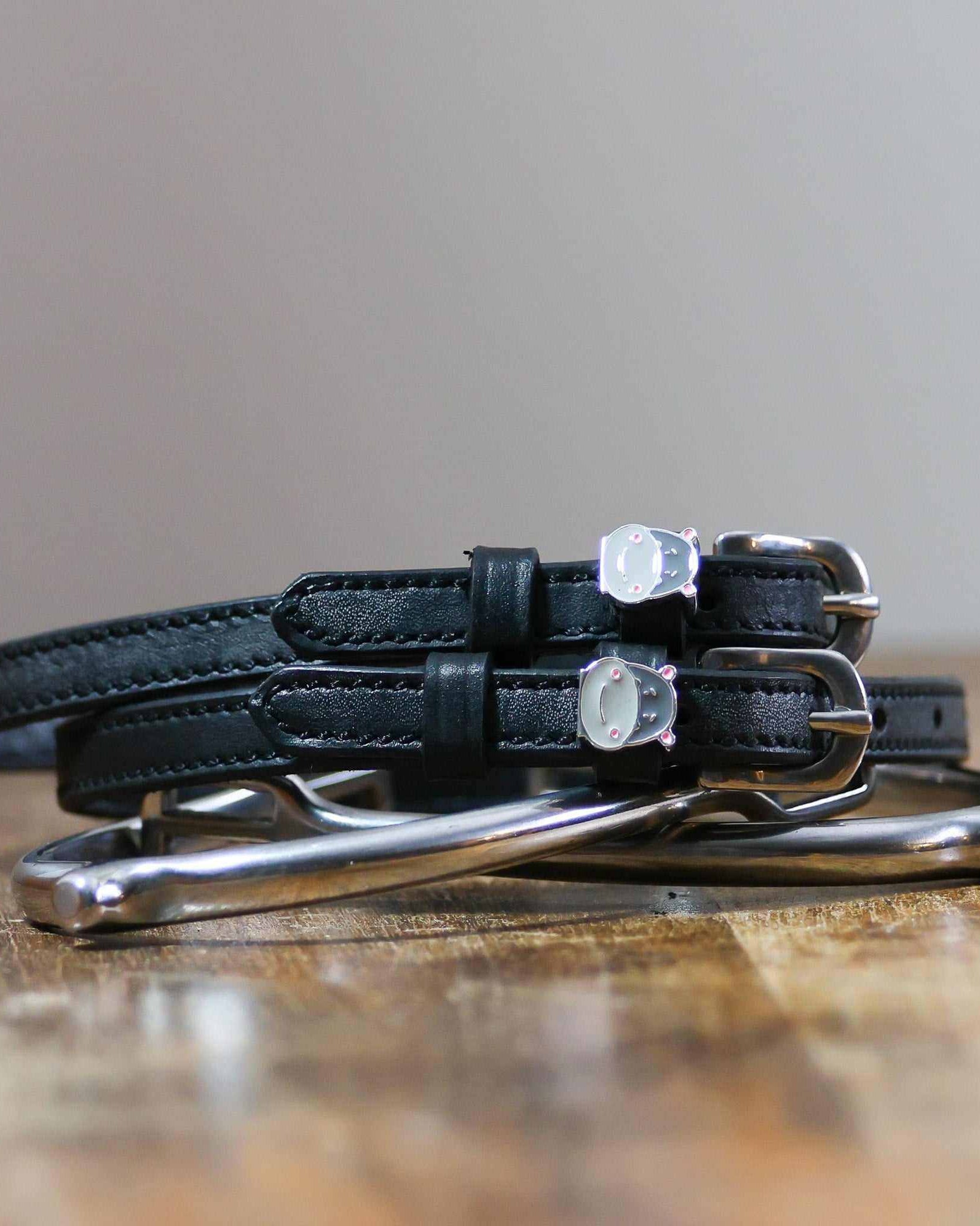ManeJane Hippo Face spur straps coiled beside silver spurs on a wooden table