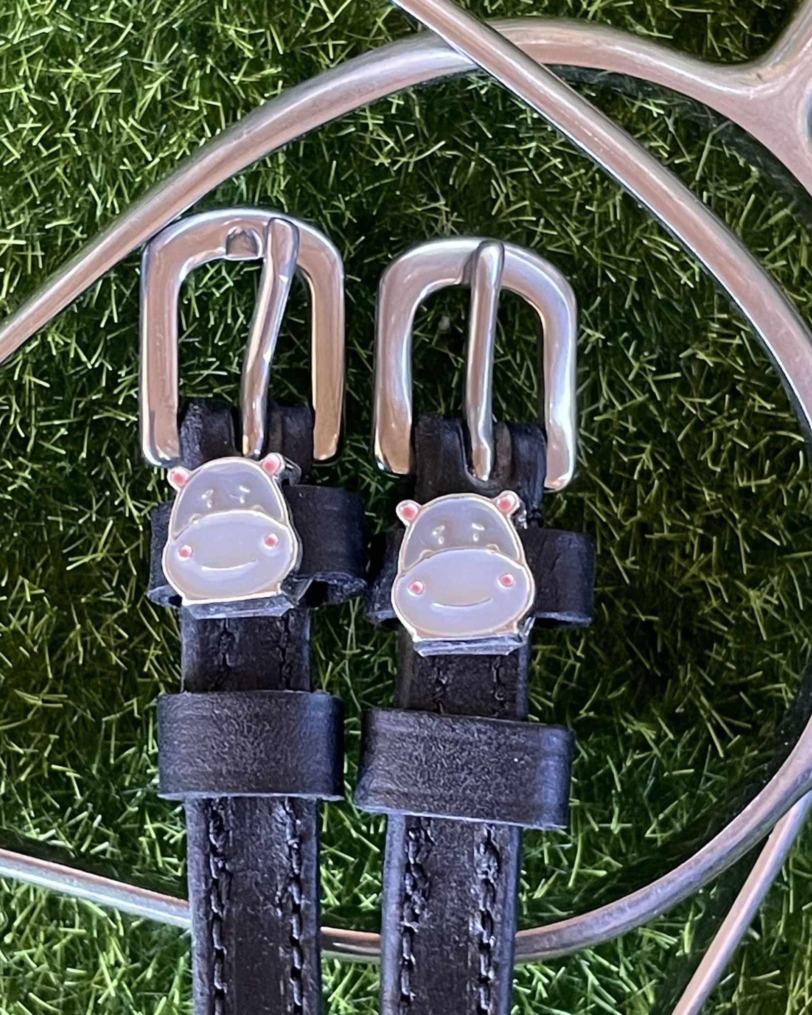 Black leather Hippo Face spur straps with silver hippo charms on grass beside a spur