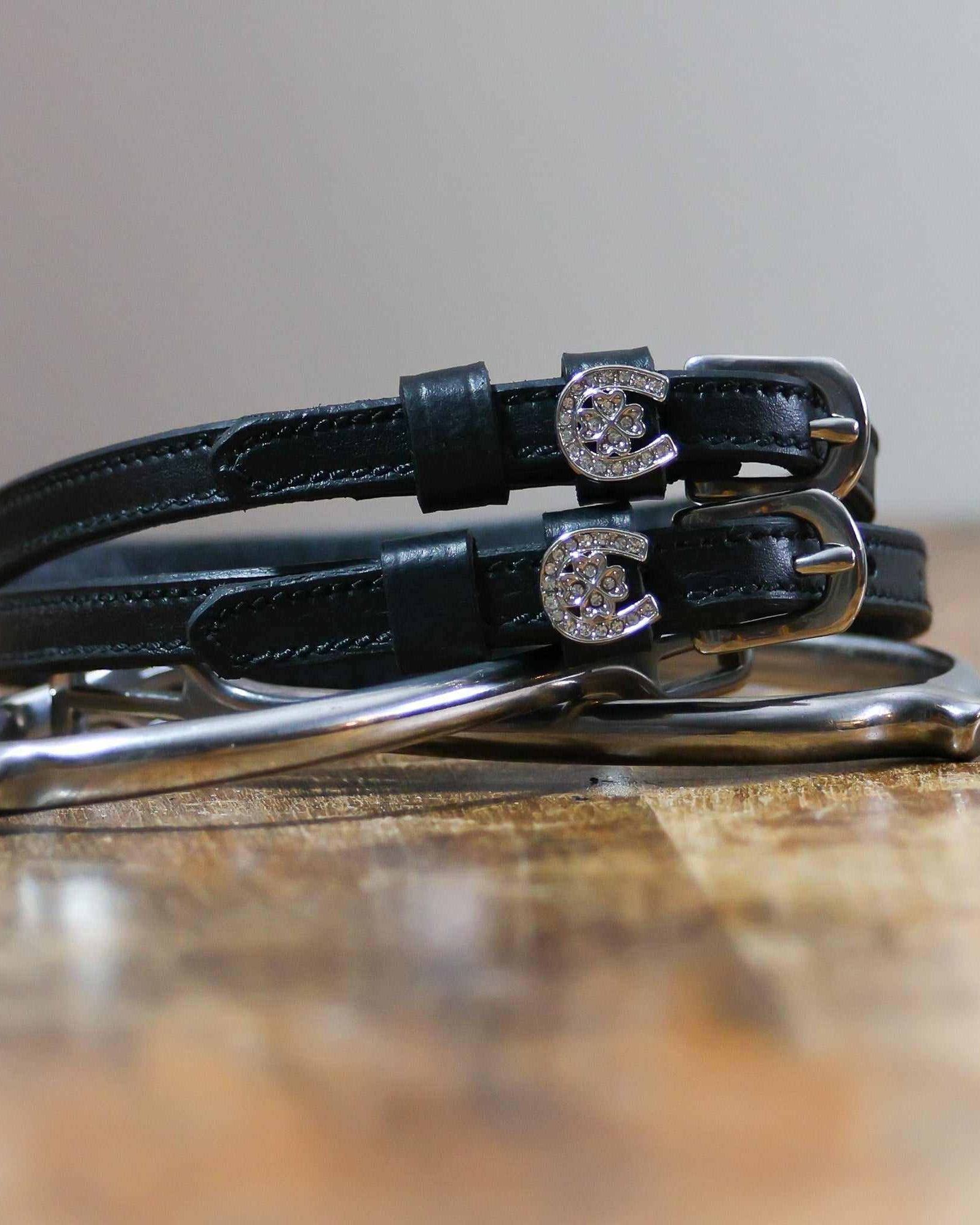 Coiled black leather spur straps with sparkling horseshoe-clover charms stacked on a spur