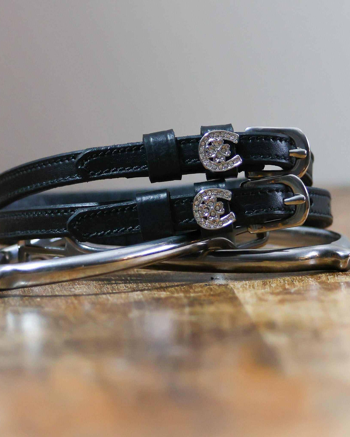 Coiled black leather spur straps with sparkling horseshoe-clover charms stacked on a spur