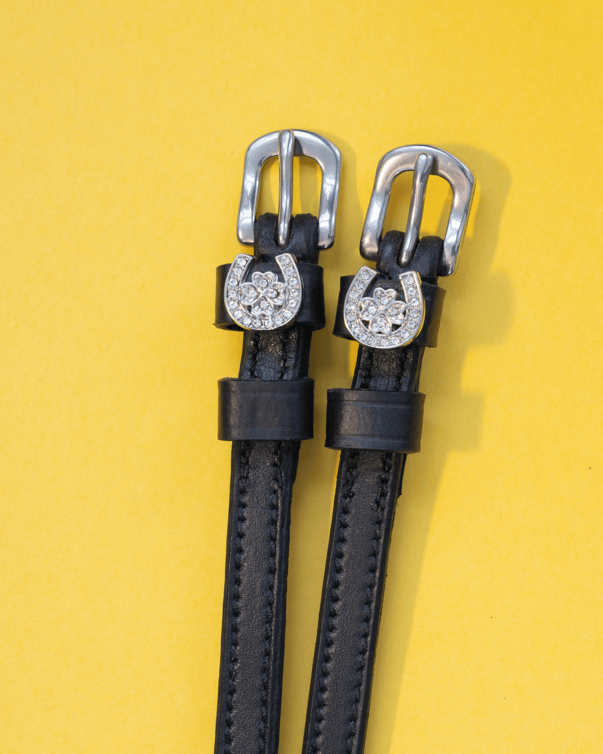 Black leather horseshoe clover spur straps with crystal charms on a yellow background