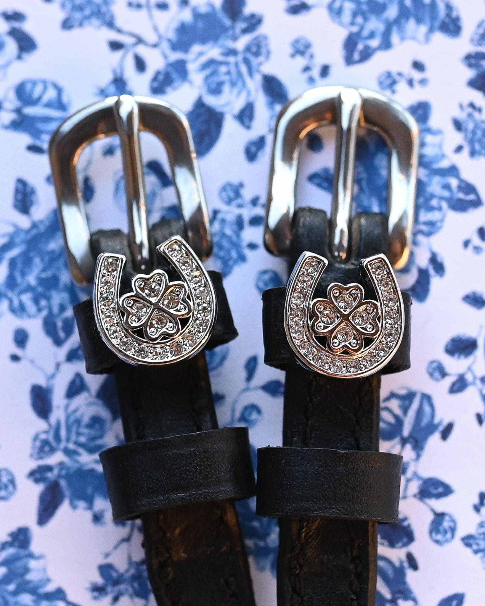 ManeJane spur straps with rhinestone horseshoe-clover charms on a blue floral background