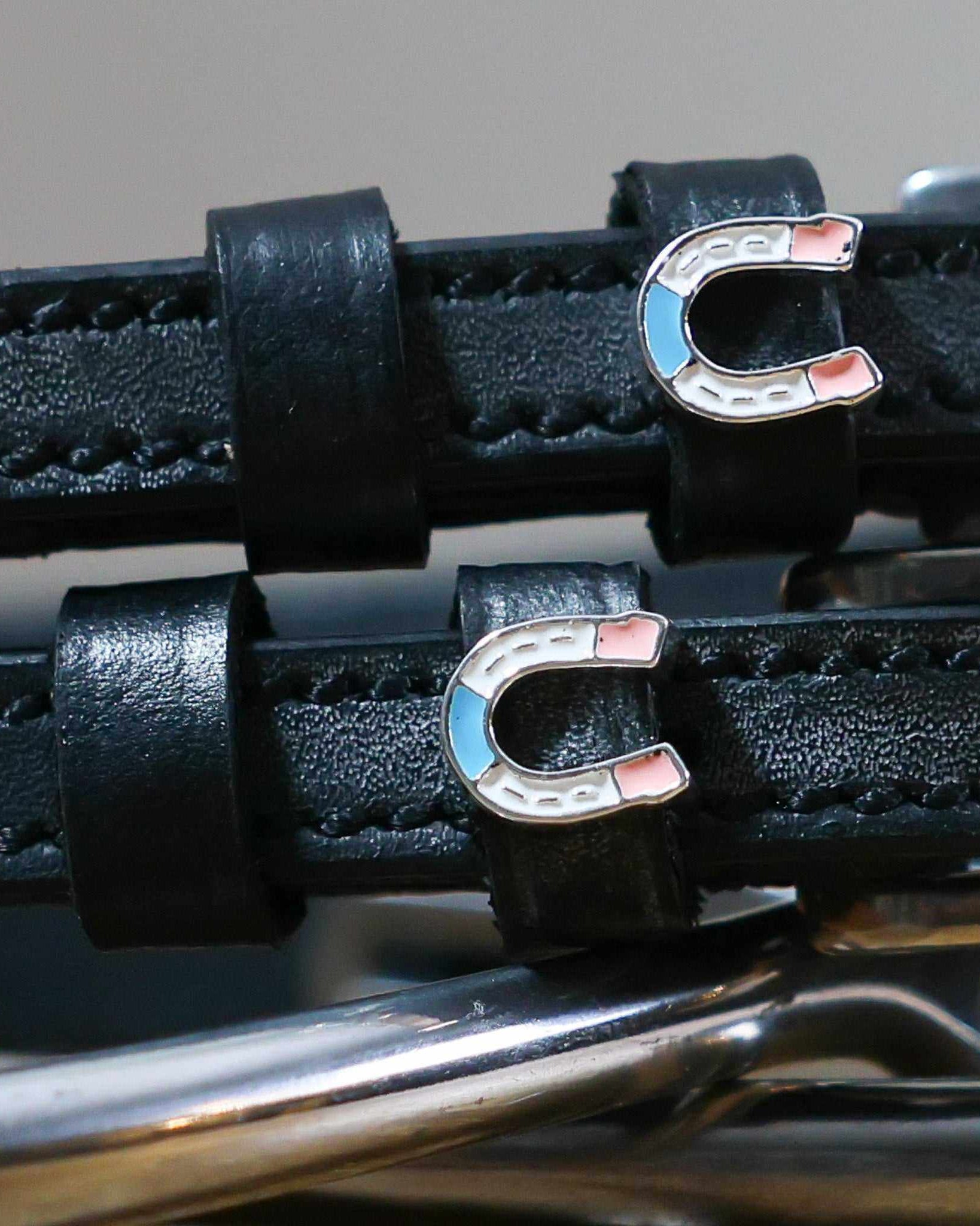 Close-up of blue-and-pink enamel horseshoe charms on black leather spur strap keepers