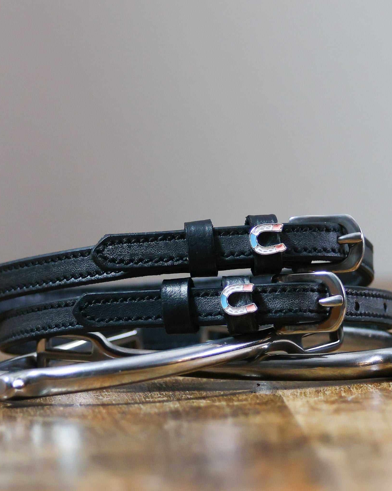 Black leather horseshoe spur straps coiled beside a silver spur on a wood surface