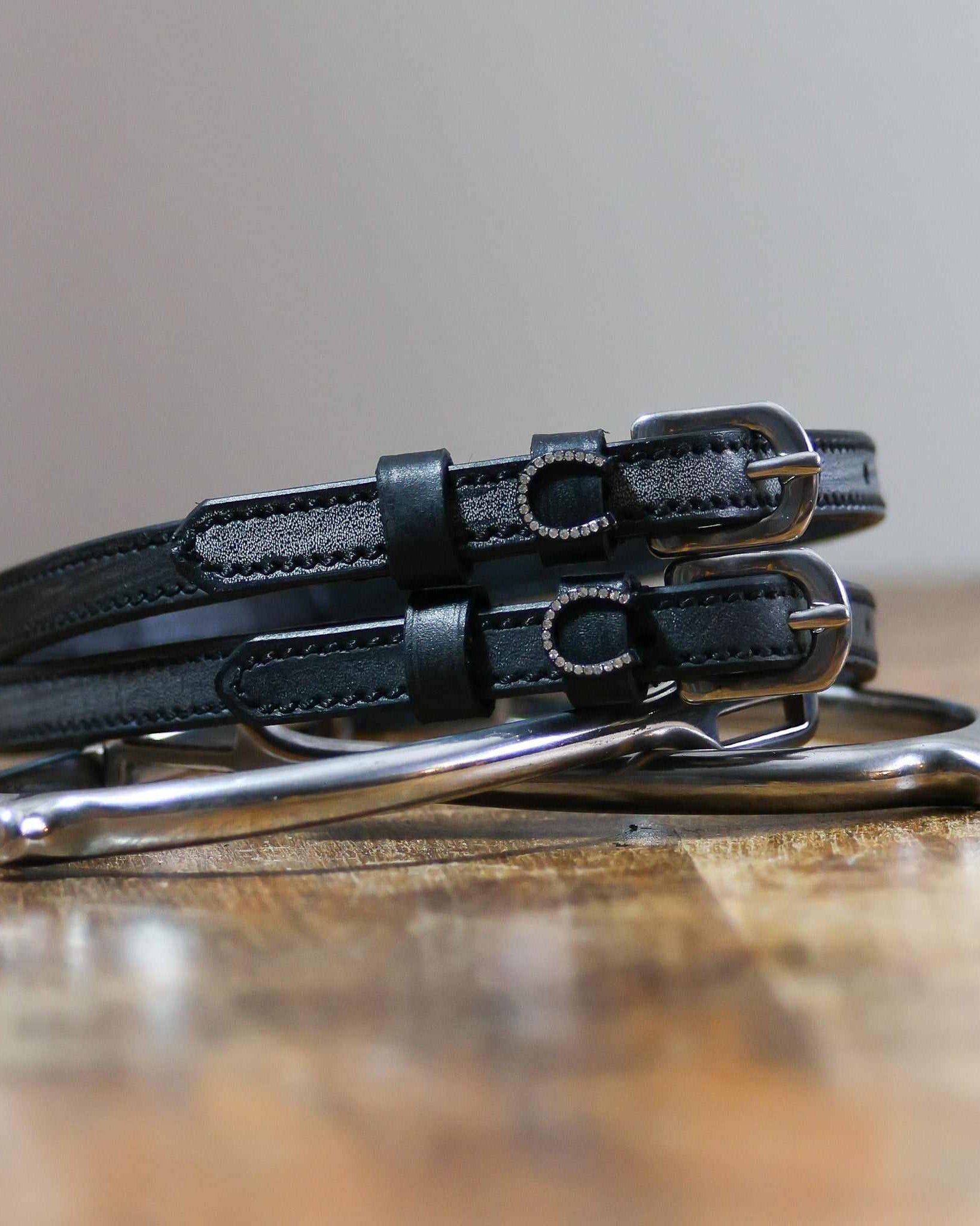 Pair of black leather spur straps coiled on wood beside a stirrup with silver bling horseshoes