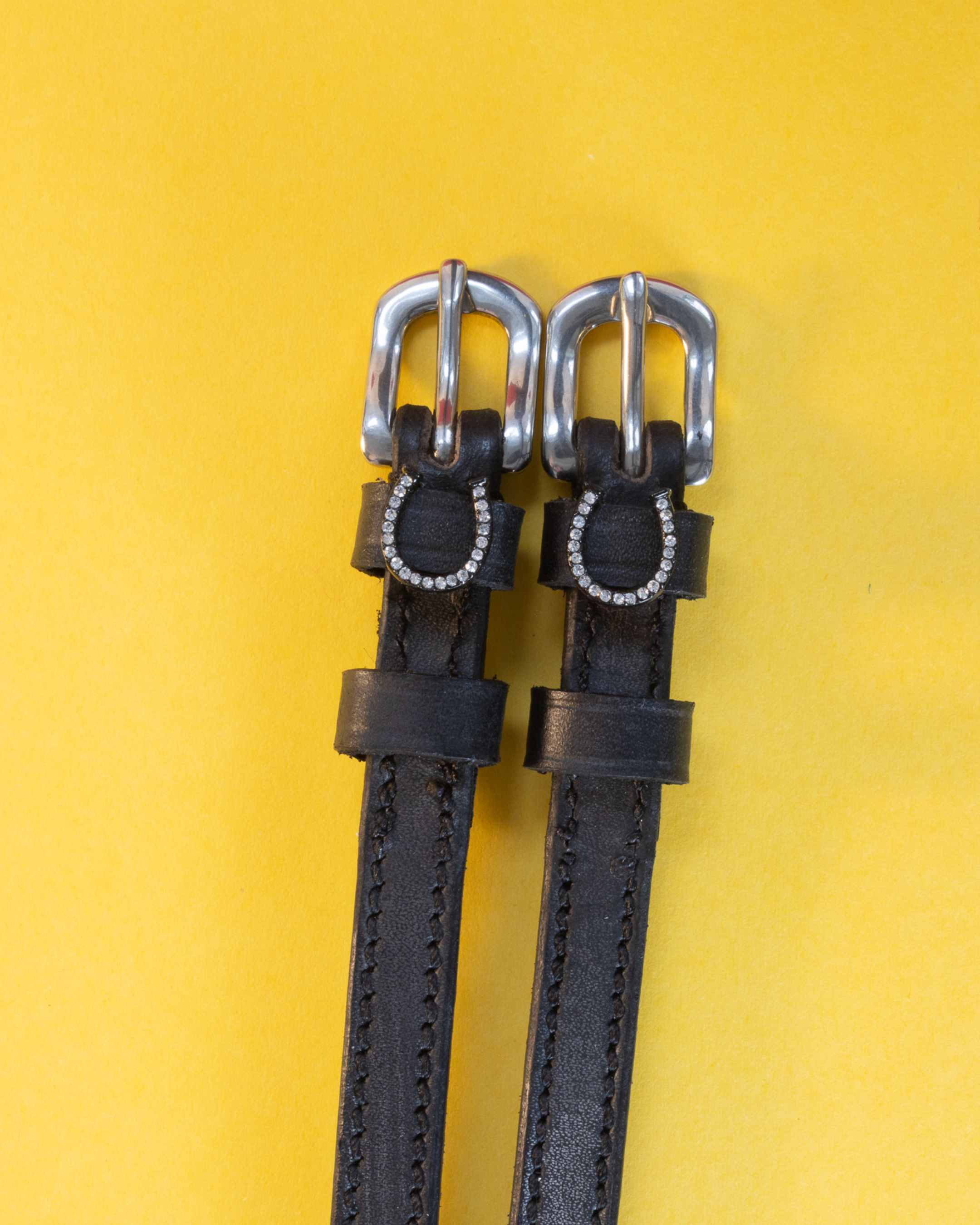 Pair of silver-bling horseshoe spur straps laid flat on a yellow background