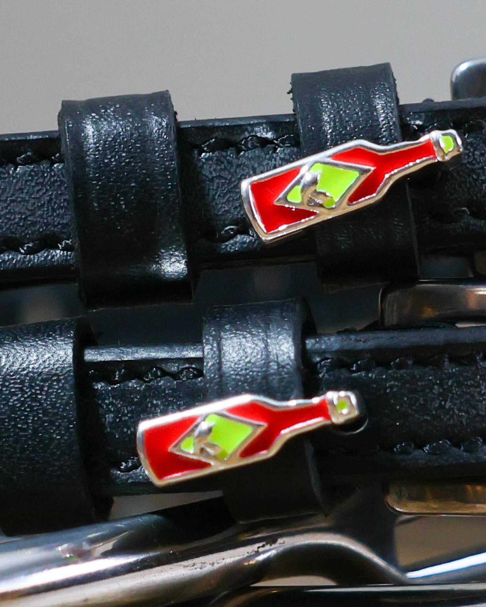 Close-up of red hot sauce bottle charms on black leather spur strap keepers