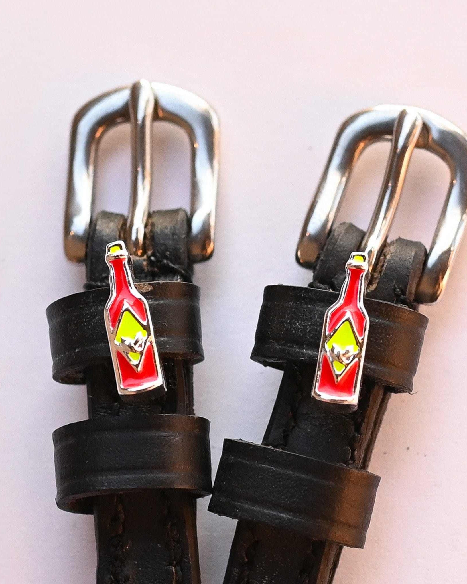 Close-up of hot sauce bottle charms and silver buckles on black spur straps