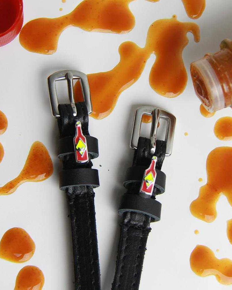 Hot sauce charm spur straps amid hot sauce splatters and a bottle on white