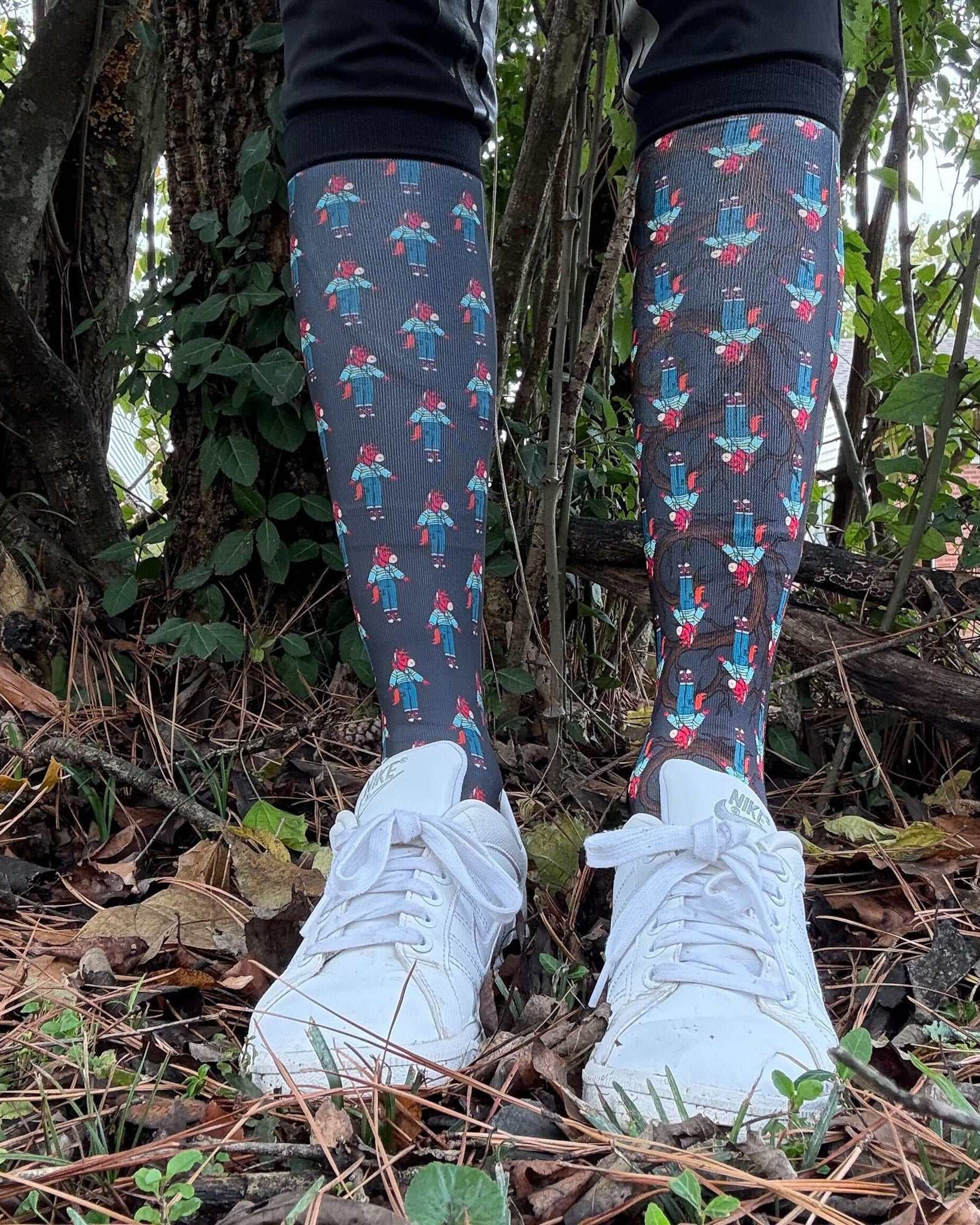 Limited Edition Trotting Up That Hill boot socks with colorful figure pattern worn with white sneakers outdoors