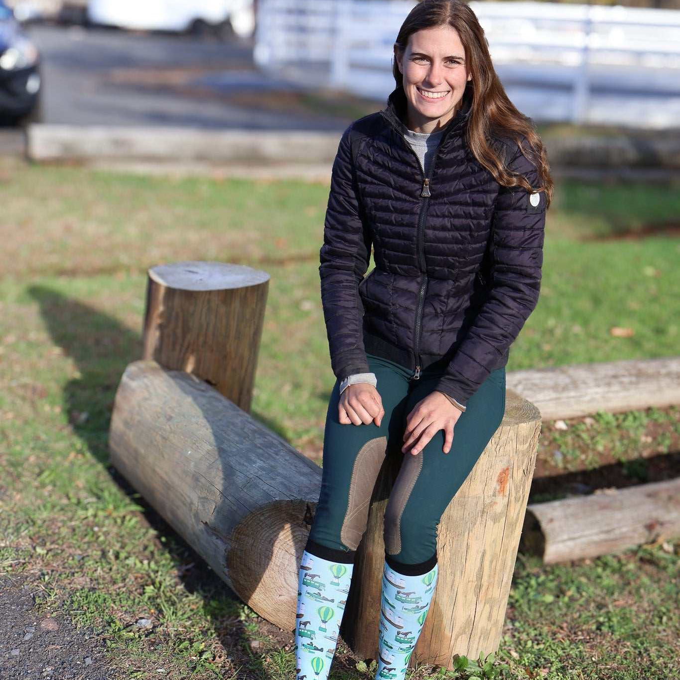 Woman sitting on log wearing Limited Edition Pony Island Pony Transport Socks with pony design in outdoor setting