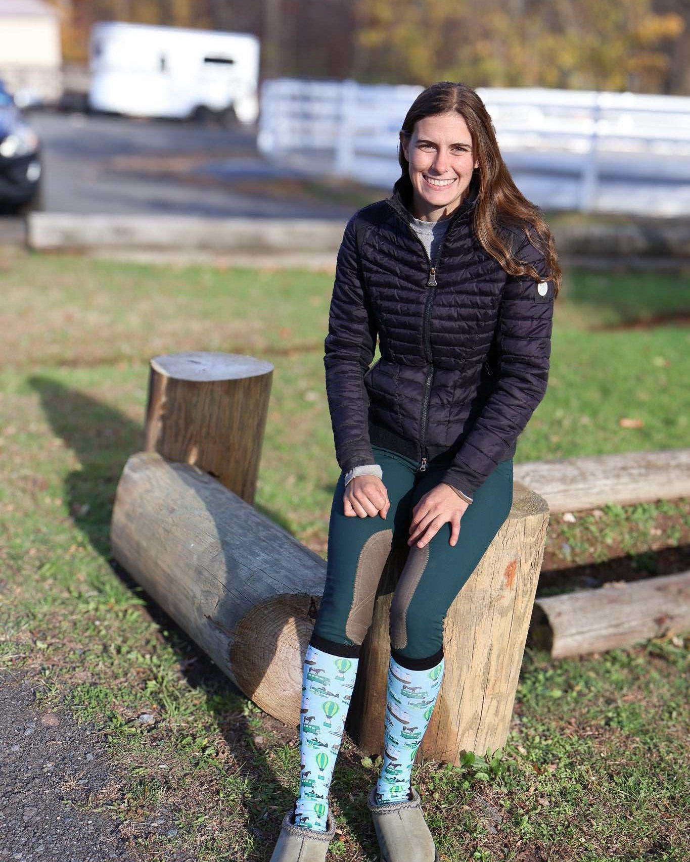 Woman sitting on log wearing Limited Edition Pony Island Pony Transport Socks with pony design in outdoor setting
