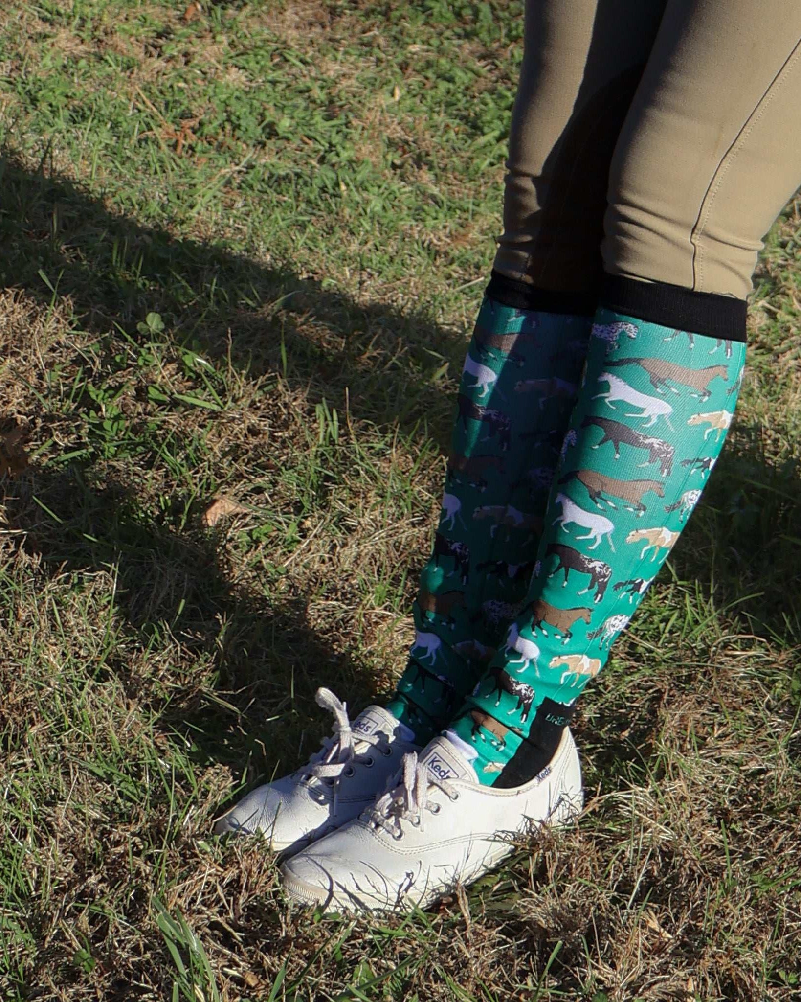 Limited Edition Pony Island green boot socks with horse pattern worn with riding pants and white sneakers outdoors
