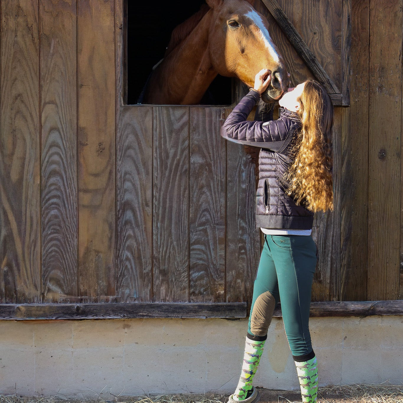 Young rider wearing Limited Edition Pony Island Neon Ponies Socks petting a horse at a stable