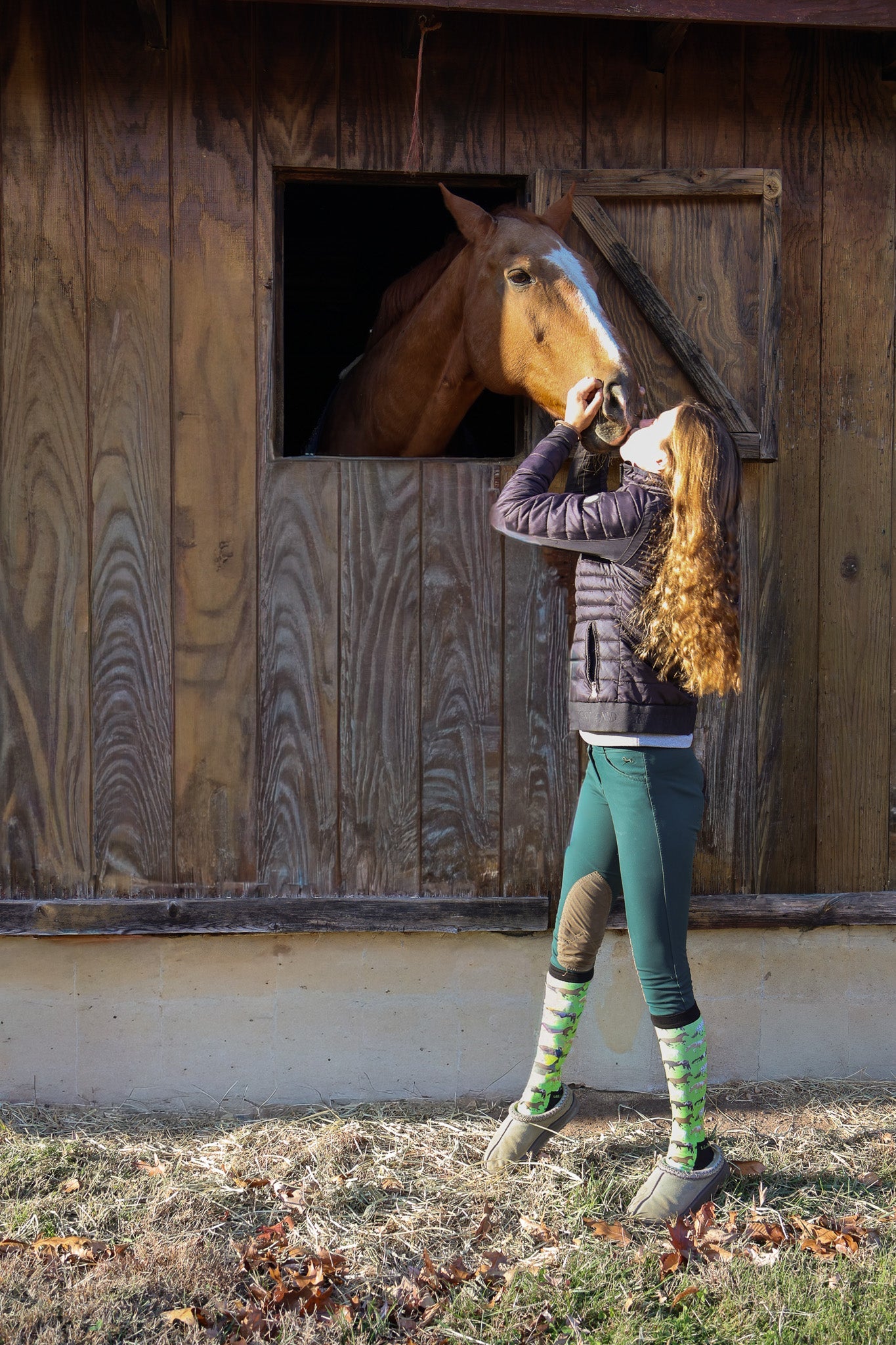 Young rider wearing Limited Edition Pony Island Neon Ponies Socks petting a horse at a stable