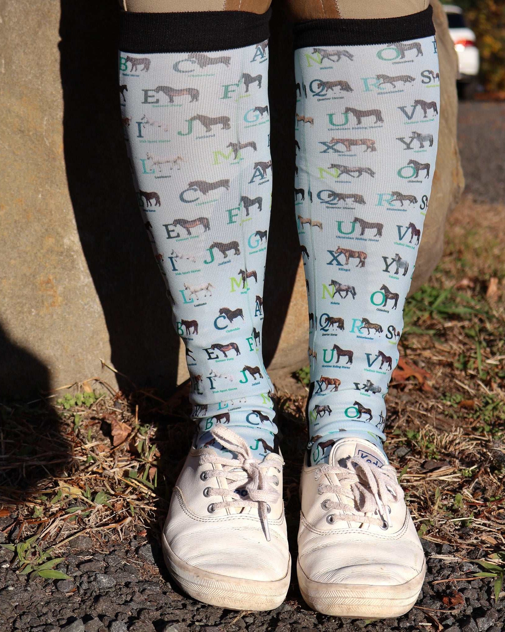 Limited Edition Pony Island Alphabet Horses socks featuring colorful horse-themed ABC design on knee-high socks worn with white sneakers outdoors